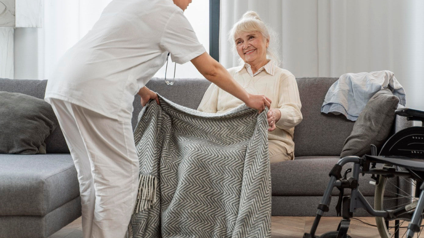 Caregiver helping an elderly woman with a blanket in a living room.